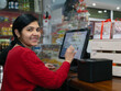 © DANILO - young smiling entrepreneur woman in apron standing in front of cash register