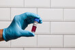 Close-up of doctor's hand wearing blue medical gloves holding a blood probe in front of a laboratory wall