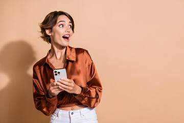 Canvas Print - Photo of dreamy exited girl wear brown blouse communicating modern gadget looking empty space isolated beige color background