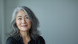 © Nataliia_Trushchenko - Happy smiling stylish confident 50 years old Asian female professional standing looking at camera at gray background. Portrait of sophisticated grey hair woman advertising products.