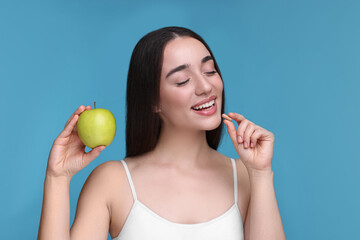 Canvas Print - Beautiful young woman with vitamin pill and apple on light blue background