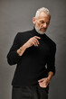 © LIGHTFIELD STUDIOS - appealing fashionable mature man in trendy turtleneck posing and looking away on gray backdrop