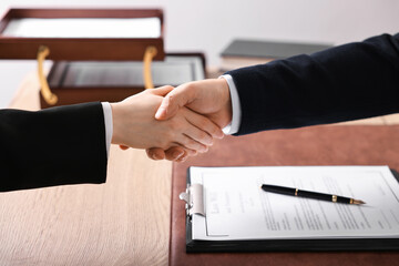 Wall Mural - Notary shaking hands with client at wooden table in office, closeup