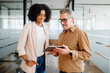 © Vadim Pastuh - A businesswoman and a senior male colleague collaboratively review content on a tablet in a bright office space, reflecting a multigenerational workplace where experience meets new technology