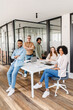 © Vadim Pastuh - A vibrant team gathers around a minimalist white table in their bright office, embodying the energy and collaboration of a modern, dynamic workplace, diverse ages and ethnic collaborate together