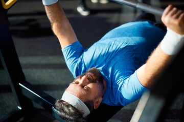 Wall Mural - Mature athlete doing strength exercises with barbell while working out in gym.