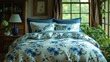 a bed with a blue and white flowered comforter and matching pillows in front of a window with potted plants.