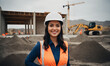 Female architect smiling. Standing at a construction site with blueprints in hand and a hard hat on her head. 