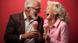 Un couple senior, heureux, amoureux, mangeant une glace, arrière-plan rouge.
