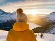 Back view image of an unrecognizable person in a yellow jacket standing and observing the view. Mountains on winter.
