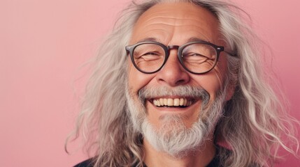 A joyful man with a long white beard and hair wearing glasses smiling broadly against a pink background.