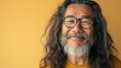 © Z A C - A man with long hair and a beard wearing glasses smiling against a yellow background.