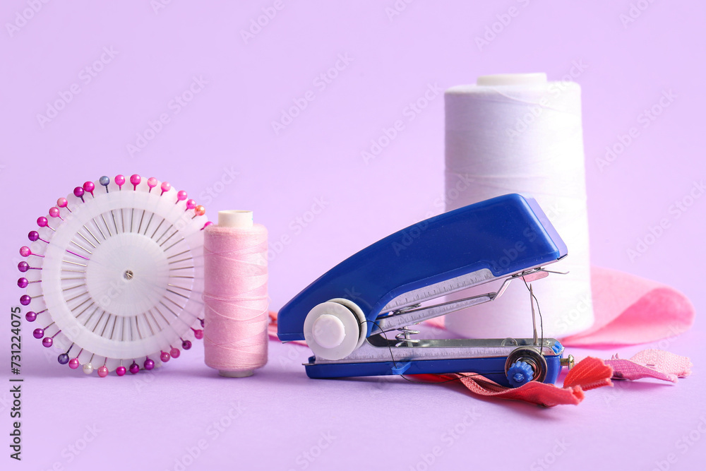 Manual sewing machine with thread spools, ball pins and zippers on lilac background