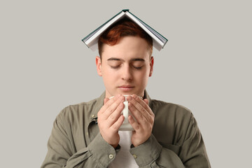 Wall Mural - Young man with cup of coffee and book on his head on grey background, closeup