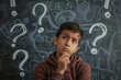 © Fabio - Concepts on blackboard at school. Hispanic boy with doubts and thoughts in class. Portrait of male child thinking against question marks on blackboard