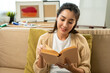 © Chanakon - Asian beautiful woman sitting reading book on cozey couch sofa in living room with sun light morning. People female stay home part time relax at home.