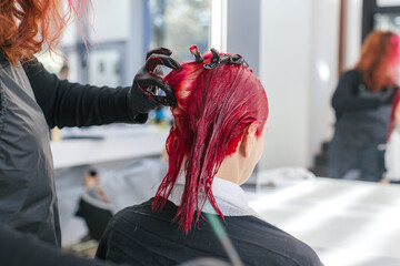 hairdresser colorist dyes a client's hair red in a hair salon.