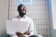 © BullRun - Smiling African American employee working with papers sitting on armchair