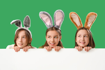 Wall Mural - Cute little girls with Easter bunny ears and blank poster on green background