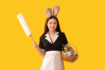 Poster - Young Asian chambermaid in bunny ears with pp-duster and Easter eggs on yellow background