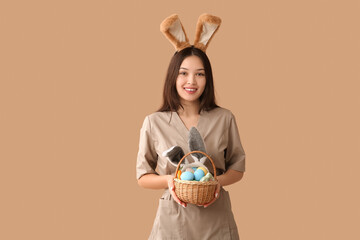 Poster - Female Asian massage therapist in bunny ears with Easter eggs on brown background