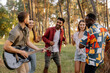 © anatoliycherkas - Multiracial group of people, bearded hipster man playing guitar and friends dancing, singing and having fun