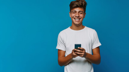 Canvas Print - young man with styled hair, smiling while looking at his smartphone against a solid blue background