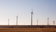 Wind turbines in a field in Kansas.  Side view. Utility lines and rural  road visible.