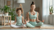 A woman and a young girl are sitting cross-legged on mats in a meditative pose with eyes closed, practicing yoga in a serene indoor environment.