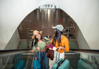 two multicultural girls going up the escalator with luggage heading to the terminal