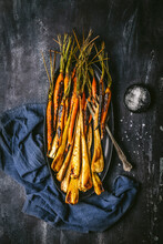 Roasted, Glazed Carrots And Parsnips Arranged On A Dark Oval Platter With Serving Fork, And Blue Linen Napkin On Dark Background