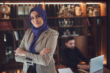 Wall Mural - Portrait of confident business Muslim woman looking at camera and standing in an office at team meeting.