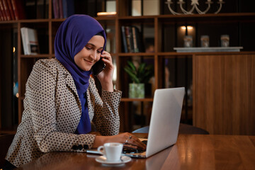 Wall Mural - Successful smiling Arab woman in hijab working inside modern office, business woman using a smart phone Muslim woman using laptop at work