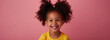 A little girl with curly hair is smiling on a pink background