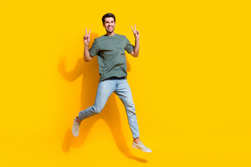 Poster - Full length photo of friendly funky guy wear khaki t-shirt jumping high showing v-signs empty space isolated yellow color background