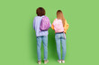 Full length rear behind photo of two young people carry backpack isolated on green color background