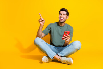 Wall Mural - Full length photo of impressed positive guy wear khaki t-shirt typing modern gadget shoving empty space isolated yellow color background