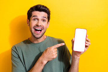 Portrait of excited guy wear stylish t-shirt indicating at eshop on smartphone screen empty space isolated on yellow color background
