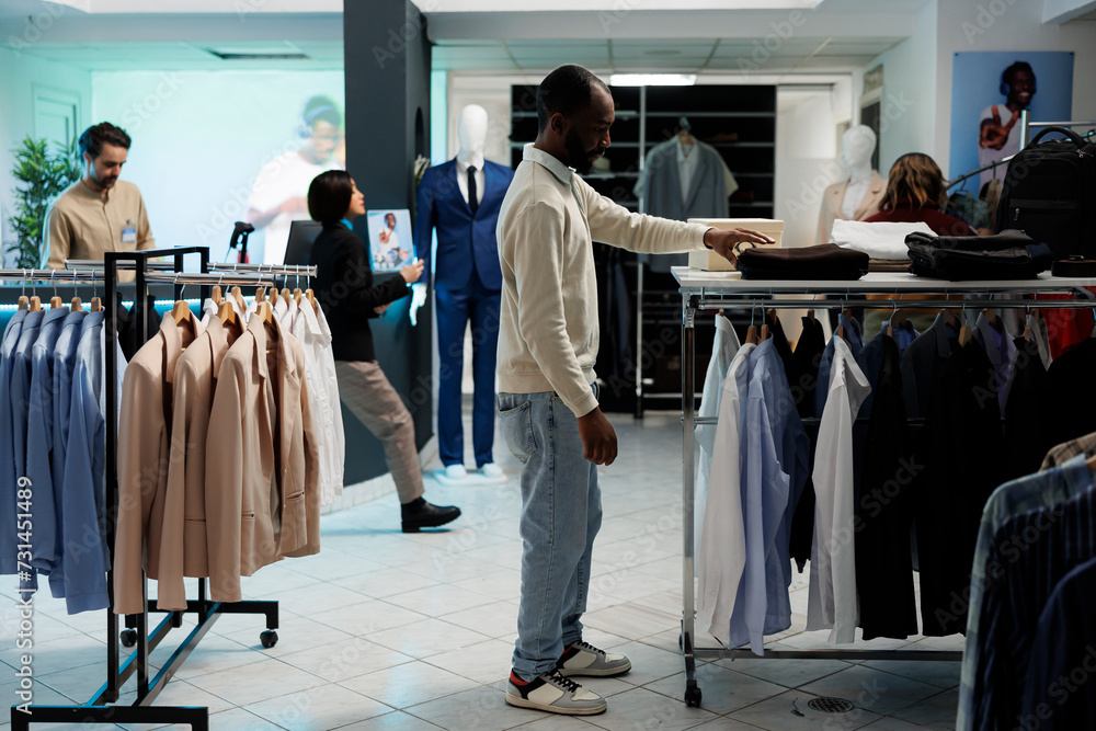 Man Browsing Racks Stylish man searching for clothes and taking apparel from shelf in ...