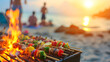 Summer bbq concept image with skewers on a hot barbecue on the beach with people in background