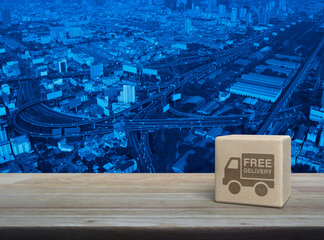 Canvas Print - Free delivery truck icon on wood block cube on wooden table over modern city tower, street, expressway and skyscraper, Business transportation service concept