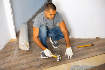 adult man installing laminate panel on substrate with technology using soft hammer while working in 