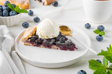 Blueberry galette, open pie or tart with ice cream and cup of tea on a white wooden table. Summer sweet pie.