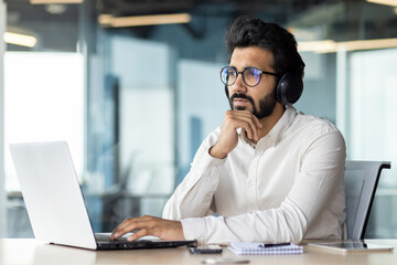 A man wearing headphones is sitting at a desk using a laptop computer