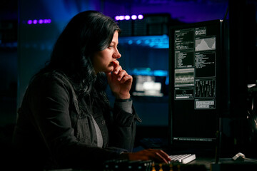 low key lighting shot of female computer hacker sitting in front of screens breaching cyber security