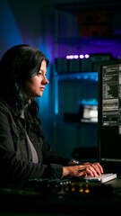 low key lighting shot of female computer hacker sitting in front of screens breaching cyber security