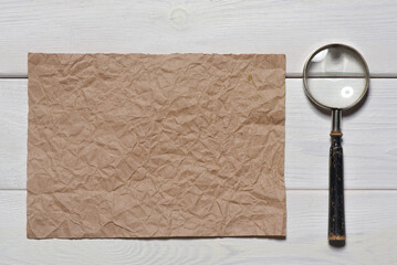 Wall Mural - blank crumpled paper sheet page and magnifying glass loupe on the wooden flat lay desk table backgro
