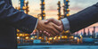 A business handshake has an industrial factory backdrop.