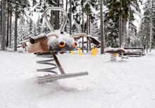 Outdoor Rocking Chair On A Spring For Children's Playgrounds In Winter On The Playground Against The Backdrop Of Snow-covered Pine Trees. Play Complex For Children.