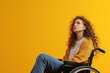 Disabled young woman in wheelchair on yellow background